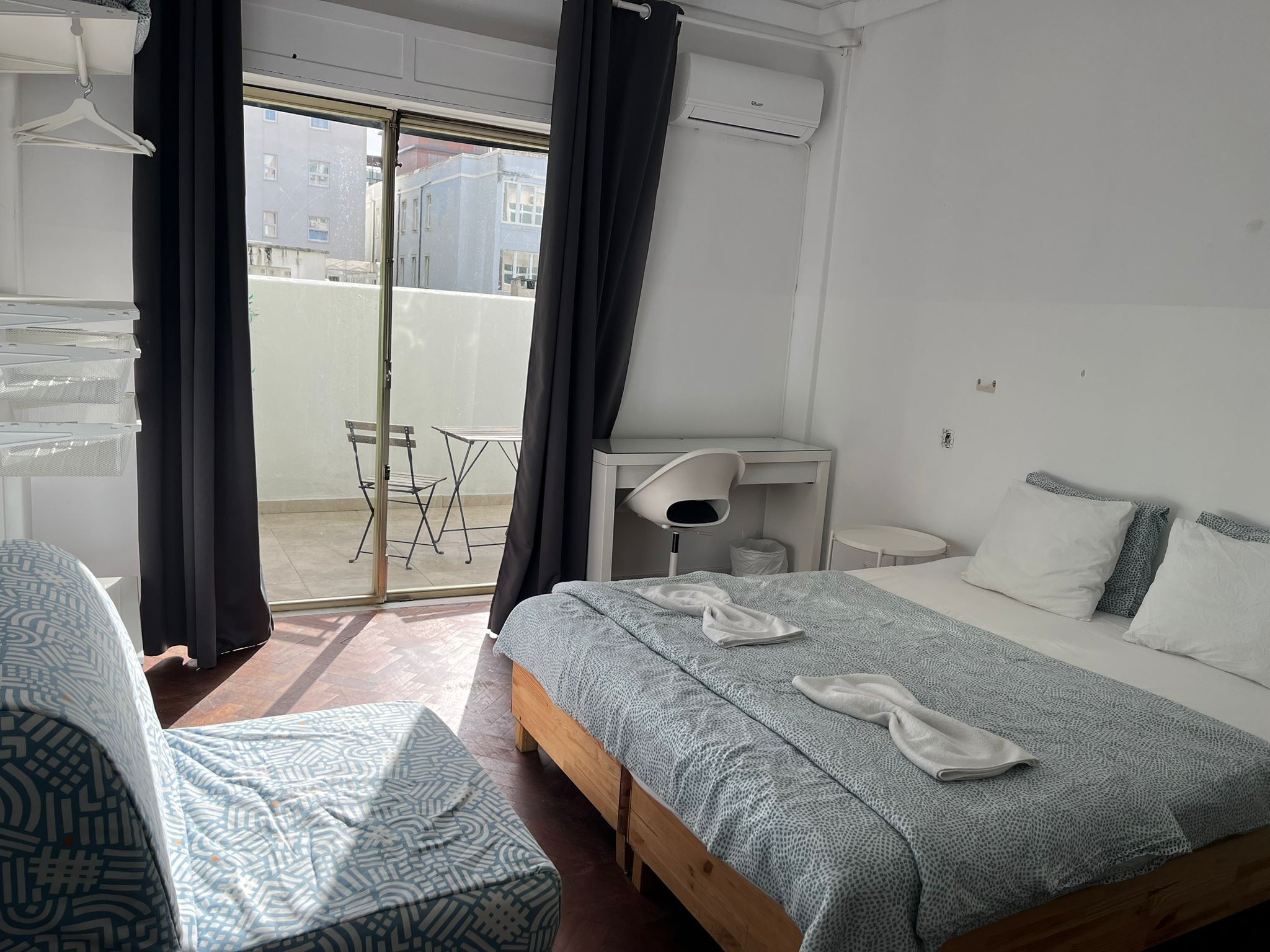 Un dormitorio con una cama, un escritorio, una silla y un balcón con mesa y sillas.