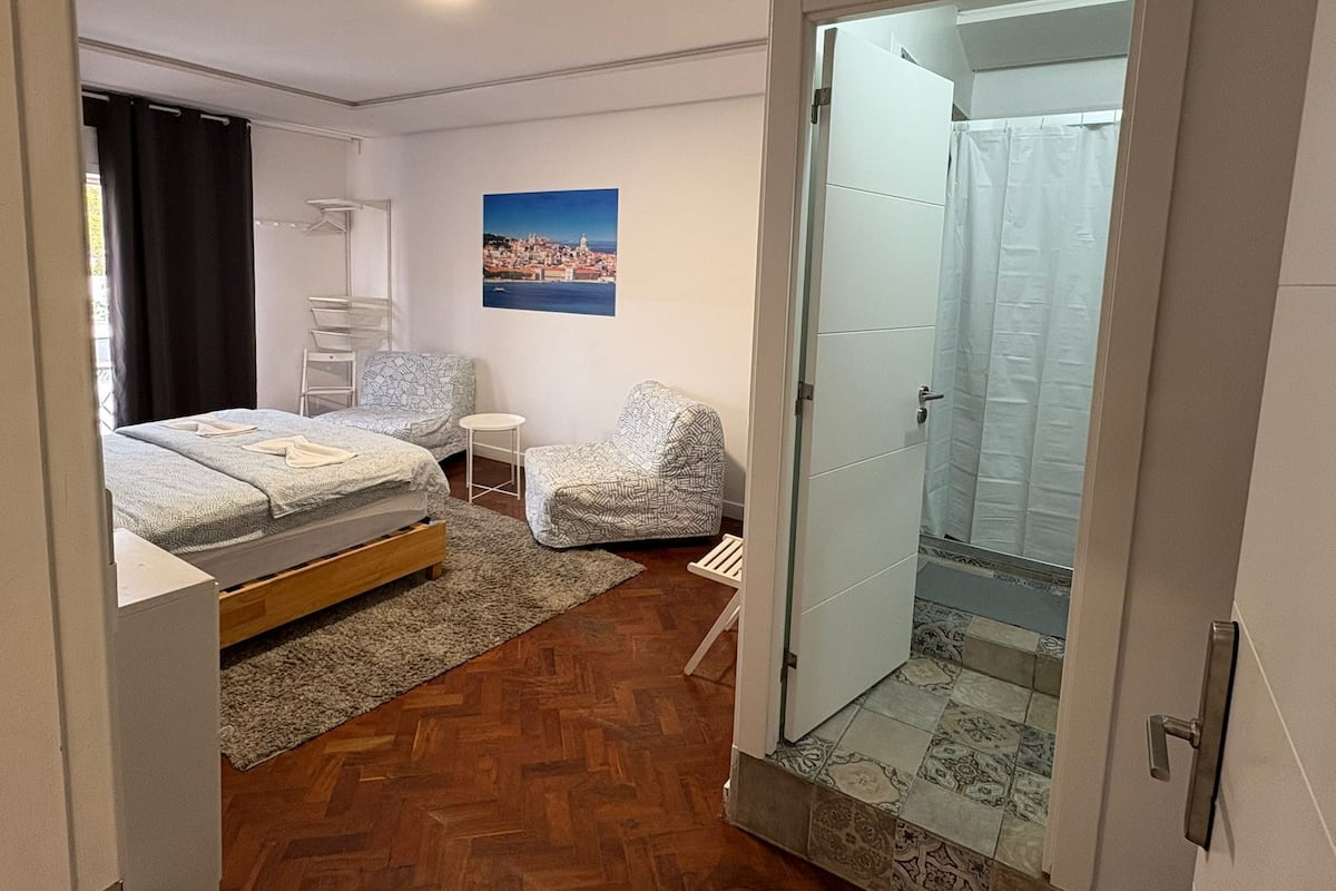 Un dormitorio con cama, una silla, una mesita, un cuadro en la pared y zona de ducha.