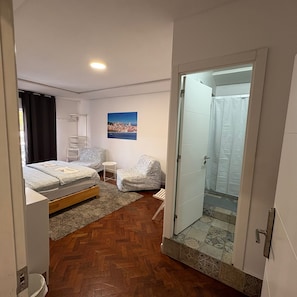Une chambre Ă coucher comprenant un lit, une chaise, une petite table, un tableau au mur et un espace douche.