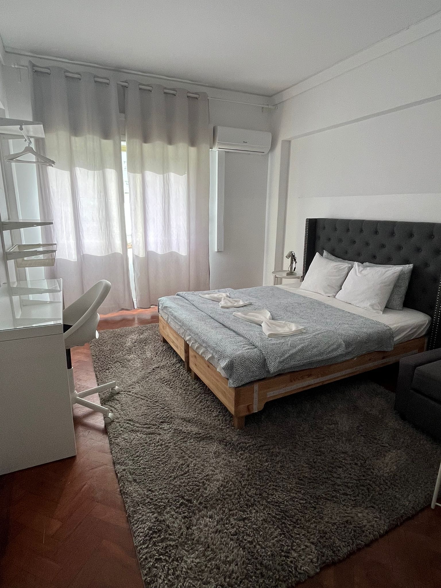 A bedroom with a bed, a desk, a chair, a nightstand, and a window with curtains.