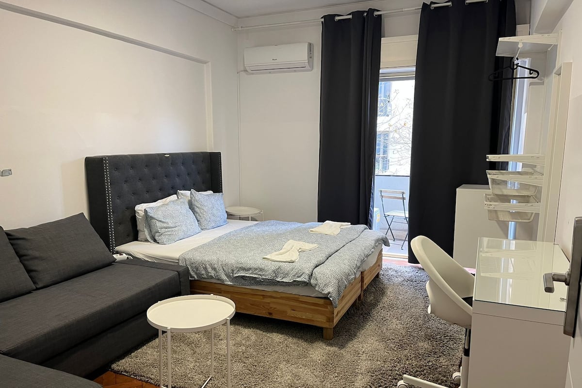 Un dormitorio con una cama, un sofá, una mesita redonda y un escritorio con una silla.