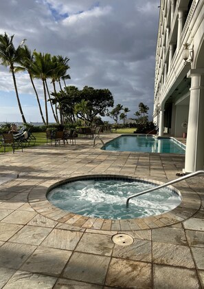 Uma área de piscina com hidromassagem, espreguiçadeiras e palmeiras.