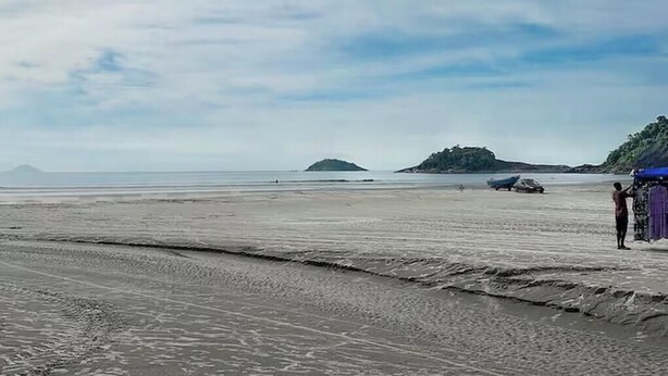 Una playa con orilla arenosa, una isla distante y una persona cerca de una estructura azul.