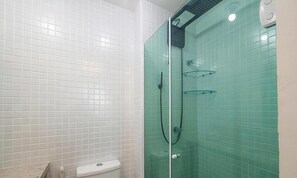 Ein Badezimmer mit weißen Fliesenwänden, einer Duschkabine aus Glas und einer Toilette.
