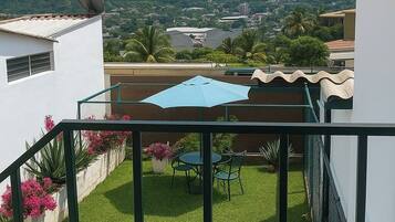 A balcony with a view of a mountain, a table with chairs, and potted plants.