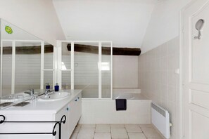 Une salle de bain avec deux lavabos, un miroir, une baignoire et un radiateur.