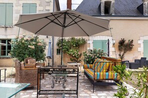 An outdoor patio with wicker furniture, a striped sofa, and a table under a large umbrella.