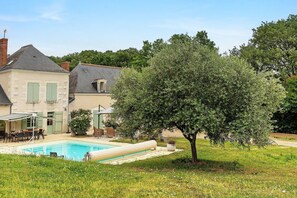 Una piscina, mobiliario de exterior y un árbol grande en un patio trasero.