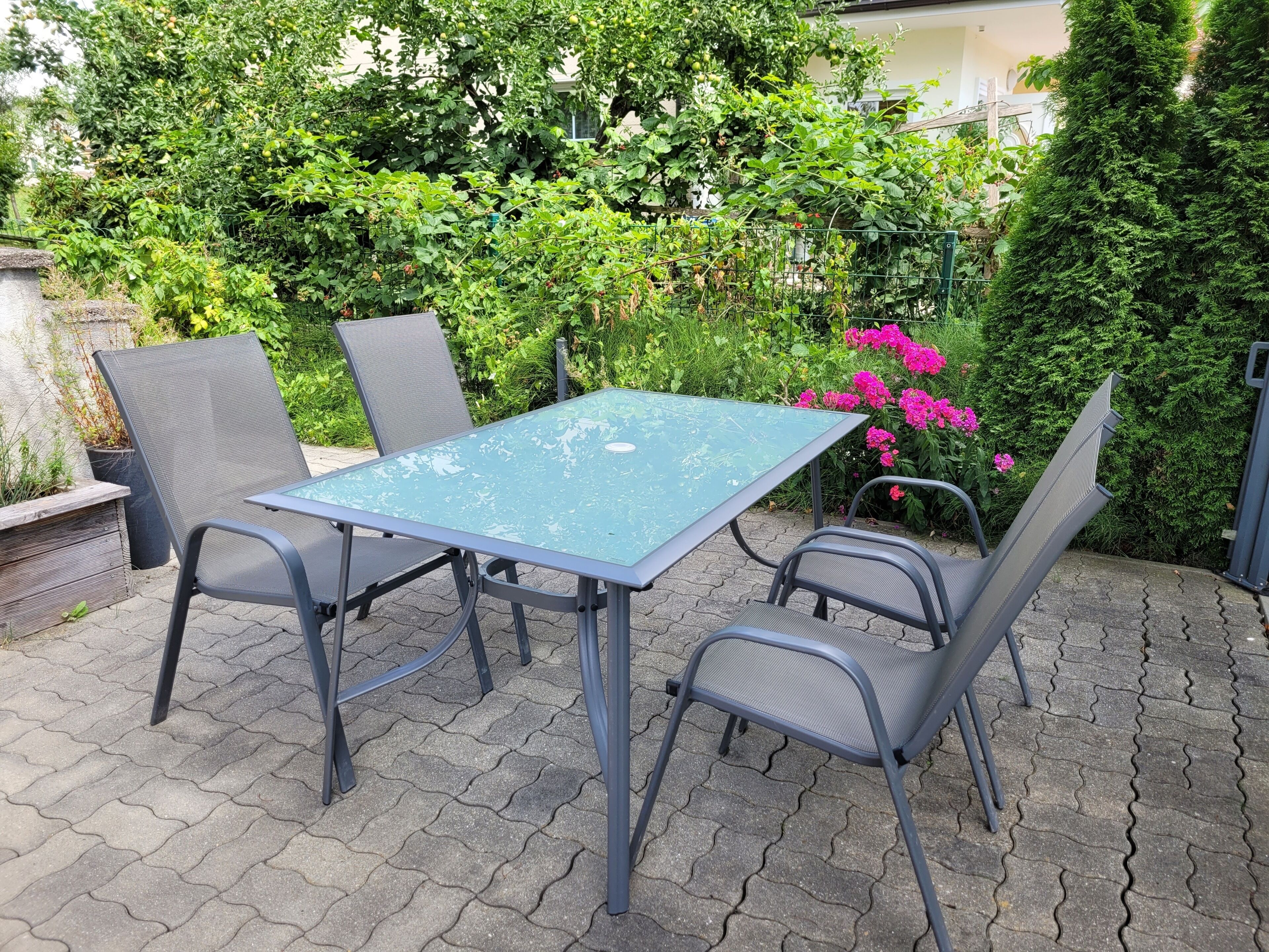 An outdoor patio with a table and chairs, surrounded by lush greenery and flowering plants.