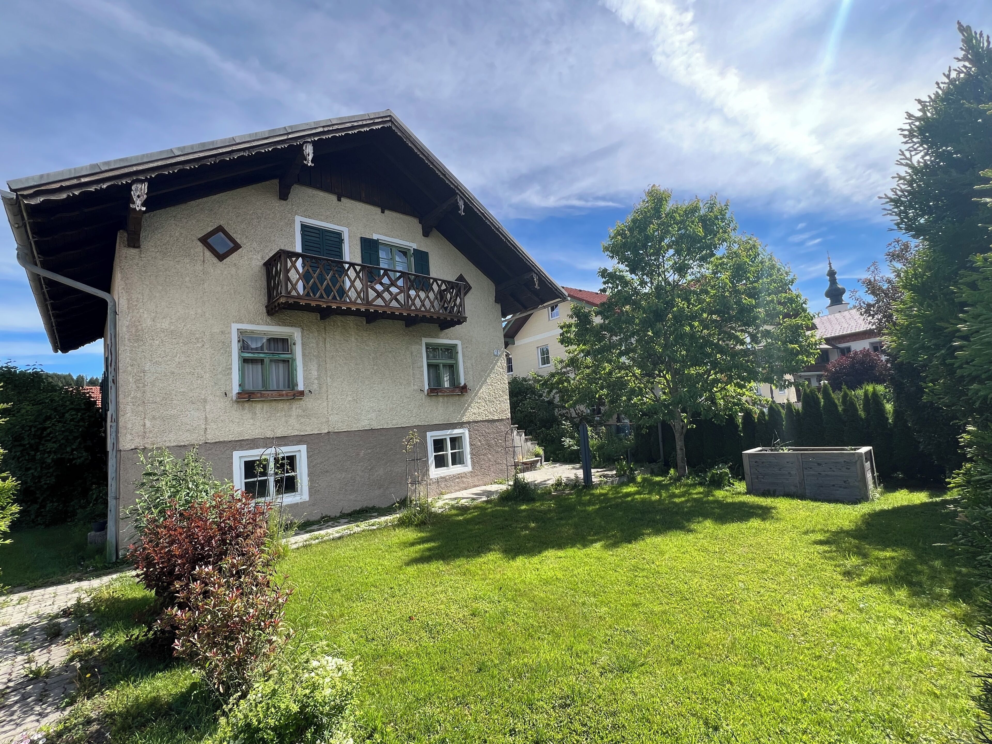 A two-story house with a balcony, a well-maintained lawn, and a garden area.
