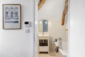 Ein Badezimmer mit Badewanne, Spiegel, Handtuchhalter, einem gerahmten Bild und einem Thermostat.