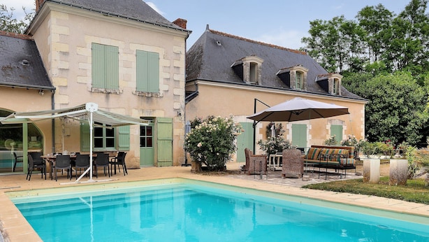 Une piscine avec un espace patio, du mobilier d’extérieur et un bâtiment doté de volets.