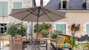 Une terrasse extérieure aménagée avec des meubles en osier, un canapé à rayures et une table placée sous un grand parasol.