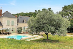 Une piscine, un espace extérieur aménagé pour s’asseoir et un grand arbre dans le jardin.