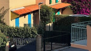 Une rangée de bâtiments de style méditerranéen, avec des toits en tuiles de terre cuite, un portail noir et une voiture garée devant.