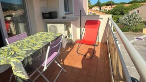 Un balcon avec une table et des chaises, une chaise rouge, un four à micro-ondes et une fenêtre donnant sur un quartier résidentiel.