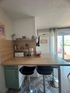 Eine moderne Küche mit Holzausziehtisch, zwei Barhocker, einer Kaffeemaschine und einem kleinen Schrank.