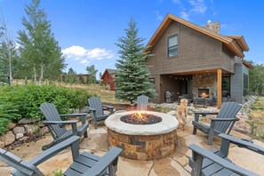 A modern house with a stone fire pit surrounded by Adirondack chairs.