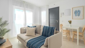 Ett modernt vardagsrum med en soffa, ett matbord med stolar, en dörr och en inramad tavla på väggen.