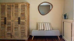 A room with a wooden wardrobe, a round mirror, a grey sofa with striped cushions, and a radiator.