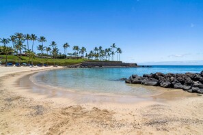 Une plage à l’eau claire, bordée de palmiers et d’une côte rocheuse.