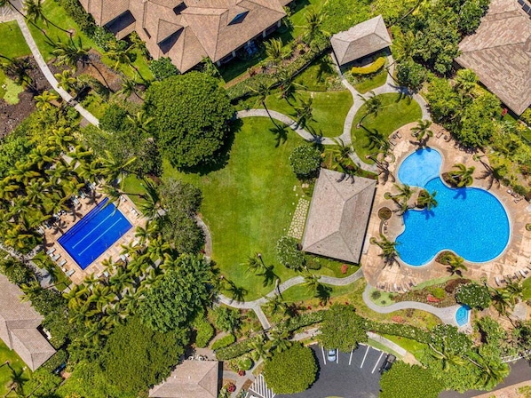 Vue aérienne d’un complexe hôtelier doté d’une piscine, d’un court de tennis et d’une végétation luxuriante.