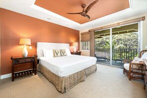 A bedroom with a large bed, two bedside lamps, a ceiling fan, a nightstand, a chair, and a balcony with a view of greenery. - Spacious Townhome With Dual Suites, Lanai BBQ & Beach Club Access (Kamuela)