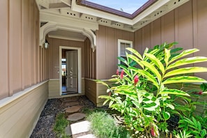 A house with a covered porch, a door, and a garden with plants and stepping stones. - Spacious Townhome With Dual Suites, Lanai BBQ & Beach Club Access (Kamuela)