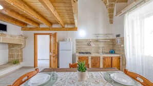 Eine rustikale Küche mit Holzbalken, einer Steinwand, einem gedeckten Esstisch und einem Blumentopf.