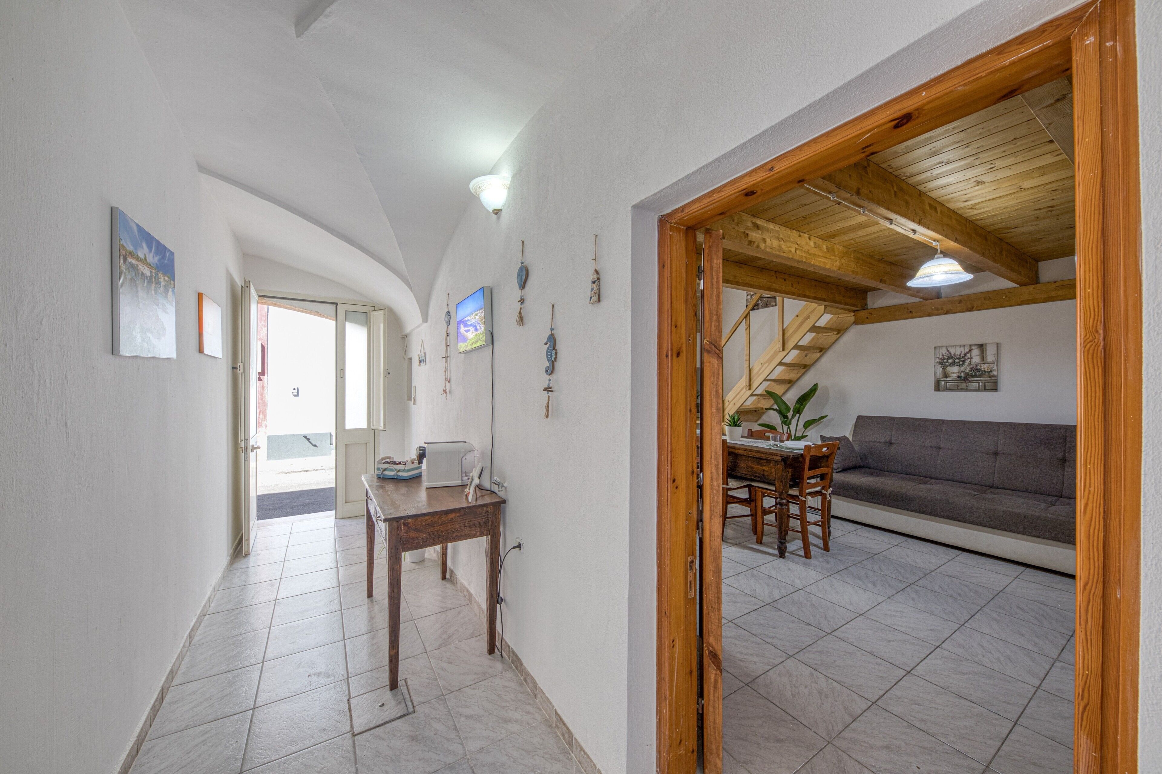 A spacious room with a wooden ceiling, a dining area with a table and chairs, a sofa, and a staircase leading to an upper level.