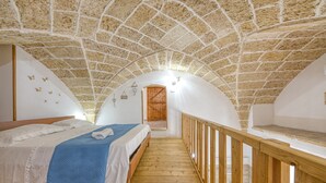 Ein Schlafzimmer mit Steindecke, Holzboden, einem Bett mit blauer Decke und einem Holzbalken.