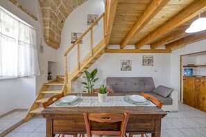 Zona pranzo con tavolo in legno, sedie, una scala, un divano e un armadio in legno.