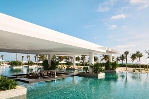 Et moderne resort med en stor, udvidende pool, palmer og en klar himmel.