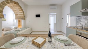 Ein Zimmer mit einem Bett, einem Esstisch gedeckt mit Tellern, Gläsern und einer Flasche, einer Küchenzeile und einem an der Wand montierten Fernseher.