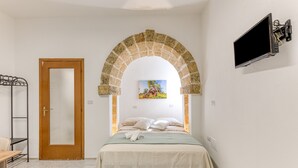 Ein Schlafzimmer mit einem Bett, einem an der Wand montierten Fernseher, einer Tür und einem darüber liegenden, gewölbten Steinbauwerk.