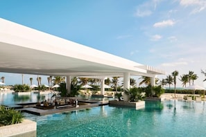 Et moderne resort med en stor, udvidende pool, palmer og en klar himmel.