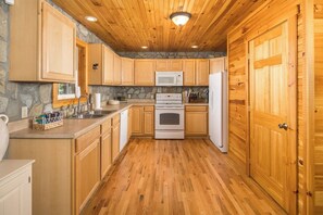 Eine Küche mit Holzausstattung, einer Steinrückwand, einer Mikrowelle, einem Backofen und einem Kühlschrank.