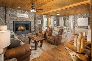 Una sala de estar acogedora con chimenea de piedra, muebles de cuero y un comedor con vistas.
