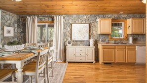 Un interior de madera con una pared de piedra, una zona de comedor con mesa y sillas, y una cocina con armarios de madera y encimera de piedra.
