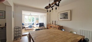 A dining area with a wooden table, chairs, a TV, and a sofa in the background. - Bright family home near the beach (Wissant)