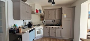 A compact kitchen with a stove, oven, and sink, light grey cabinets, and a small countertop with various items. - Bright family home near the beach (Wissant)