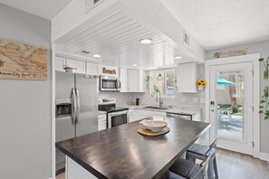 Een moderne keuken met witte kasten, een centraal eiland, roestvrijstalen apparatuur en een kaart aan de muur.