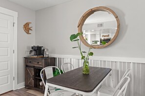 Ein Essbereich mit einem Holztisch, weißen Stühlen, einer Kaffeestation und einem Spiegel an der Wand.