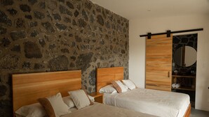 A bedroom with two wooden beds, a stone wall, a wooden wardrobe, and a mirror.