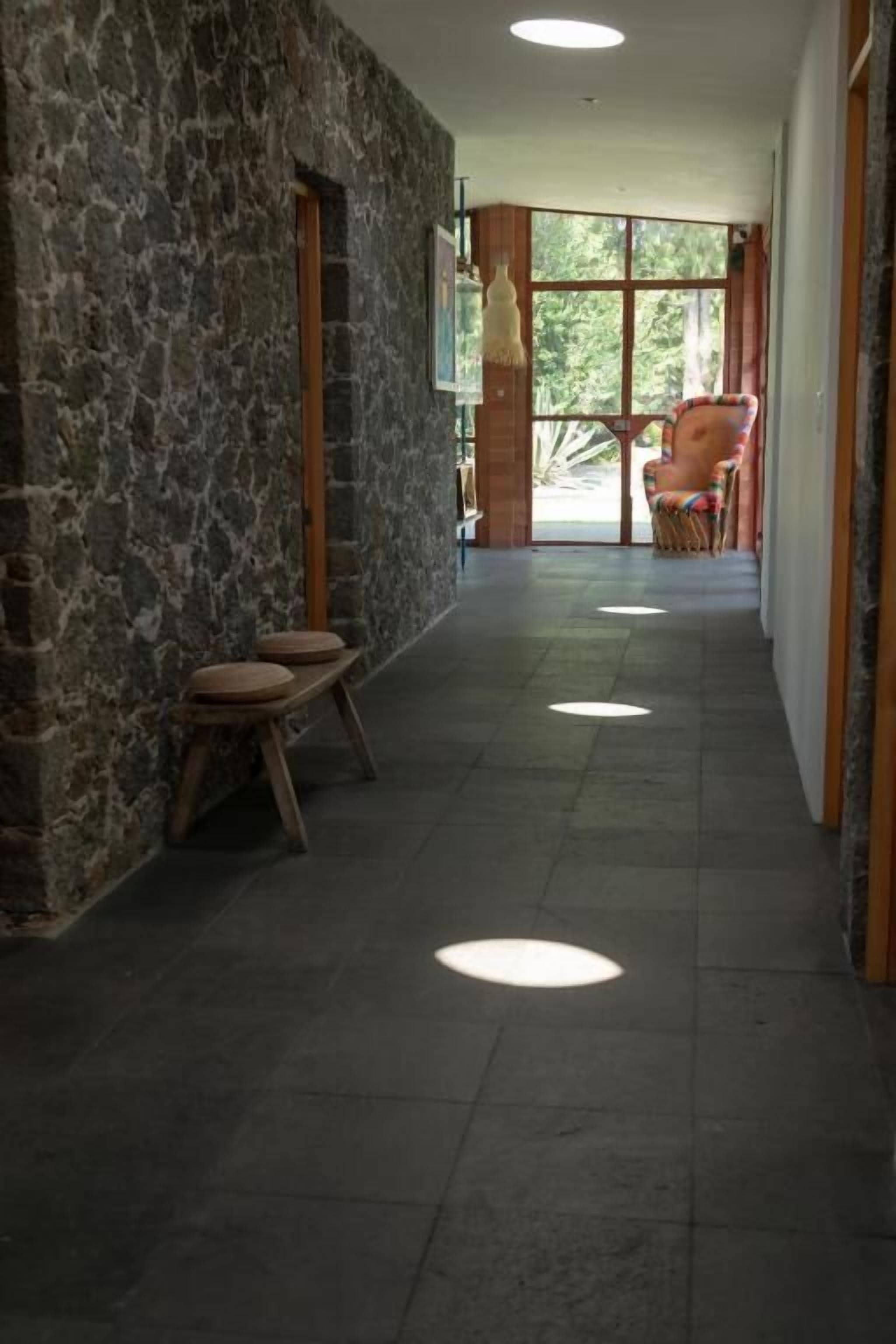 A hallway with stone walls, a wooden bench, and a view of the outdoors through large windows.