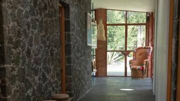 A hallway with stone walls, a wooden bench, and a view of the outdoors through large windows.