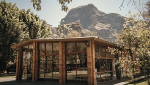 A glass-enclosed pavilion with brick pillars, surrounded by trees and a mountain backdrop.