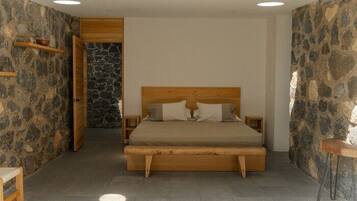 Un dormitorio con una cama de madera, paredes de piedra y una pequeña mesa de madera.