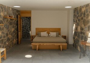 Un dormitorio con una cama de madera, paredes de piedra y una pequeña mesa de madera.