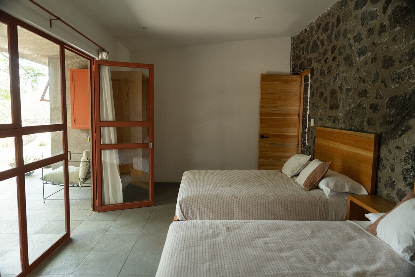 A bedroom with two beds, a wooden wardrobe, and a sliding glass door leading to an outdoor area.
